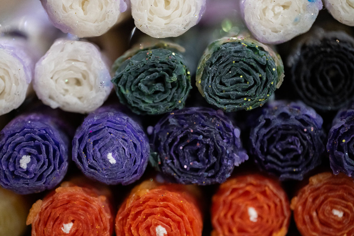 Colourful rolled beeswax candles in shades of purple, green, cream, and orange at Mercurius Curio Shop.